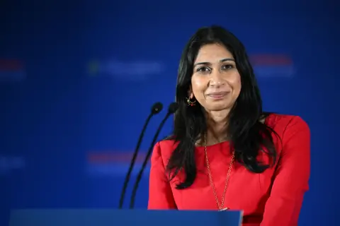 Suella Braverman looks into the camera while standing at a podium. 