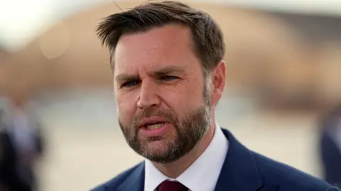 Reuters JD Vance, speaking while wearing a white shirt, dark blue jacket and dark tie