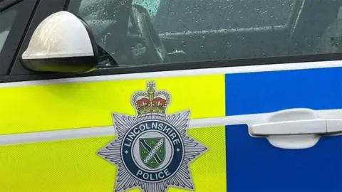 The side of a yellow and blue marked Lincolnshire Police car showing the force's badge