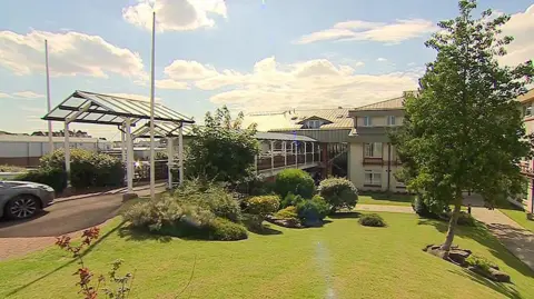 The three-storey Sandpipers hotel in Southport has a neatly cut lawn, shrubs and trees in a garden area to the front.