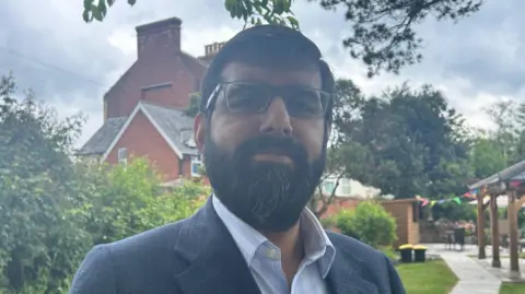 A man with a beard and glasses wearing a blue suit looking at the camera
