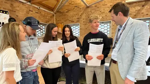 Julia Gregory/BBC A male and a female teacher either side of four pupils who are holding their results