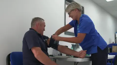 Farmer Roland Nancekivell is pictured having his blood pressure checked by market nurse Buffy. They are both smiling.
