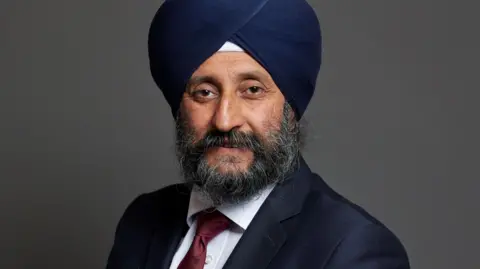 UK Parliament A man wearing a white shirt, reed tie, suit jacket and navy blue turban