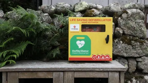 Inga Drazniece A yellow defibrillator on top of a double wooden bin. 