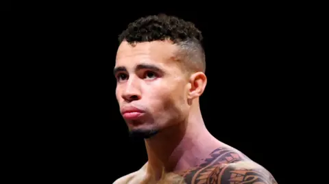 Getty Images A man with shoulder and neck tattoos visible in tribal motifs. He is against a black background