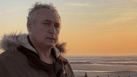 Fintan McDwyer standing in front of a beach at sunset