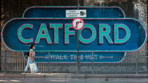 Getty Images A blue mural with the word 'Catford' behind a woman walking past and a traffic enforcement cameras and no right turn sign