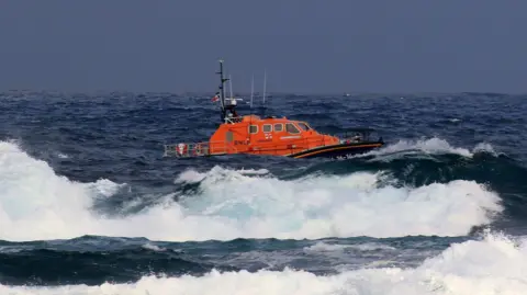 The RNLI Tamar class lifeboat 'City of London III' in rough seas. The orange and black lifeboat riding the waves.