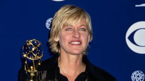 Getty Images Ellen DeGeneres with her Emmy award, wearing a black shirt and black jacket