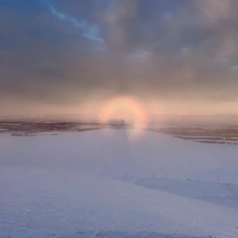 Anna Tully The Brocken spectre appears as a large shadowy figure with a bright halo. The hilltop is covered in snow.