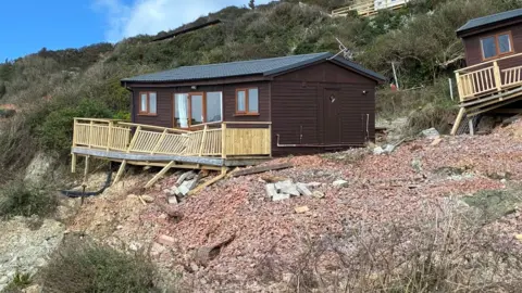 A holiday chalet in Branscombe with legs on the decking area having given way after a landslip.