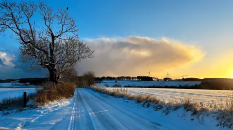 BBC Weather Watchers/C Bee A snow covered road by fields with wind turbines in the background 