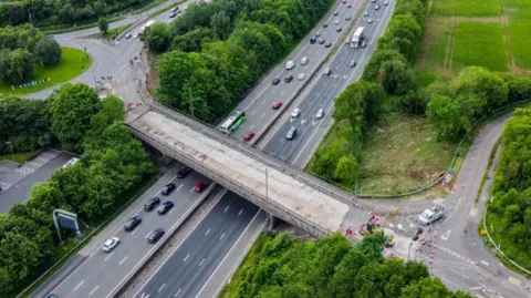 A drone image of a bridge over the M4 motorway. Cars are driving underneath the bridge which is undergoing repair work