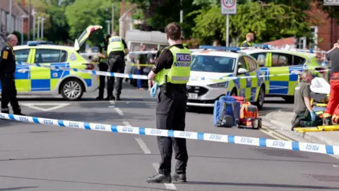 Media News GNP Ltd A police officer stands in front of blue and white tape while paramedics and their bags are on the pavement in the background are a number of police cars