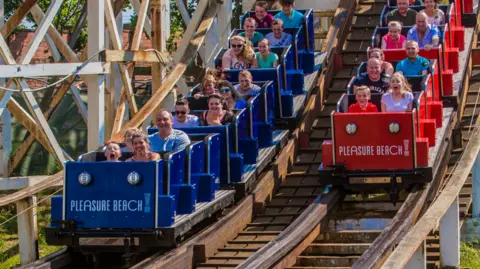 Stephen Lee Image shows the red and blue carriages of the Grand National at Blackpool Pleasure Beach. They are racing along the timber-framed rollercoaster's track. 
