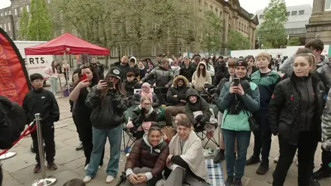Scores on people on the Flag Market in Preston waiting by the food truck. Many are holding phones taking pictures