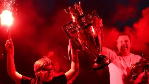 Getty Images Two Liverpool fans celebrate with replica Premier League trophy outside Anfield