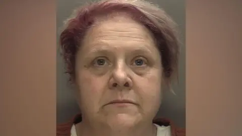 West Midlands Police A custody image of Deborah Latewood, a woman with short hair that is purple at the front and grey at the back. She is stood against a grey background