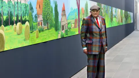 David Hockney/Getty Images David Hockney in checked suit and hat posing in front of his painting "A year in Normandy", a colourful work showing landscape of Normandy in seasons