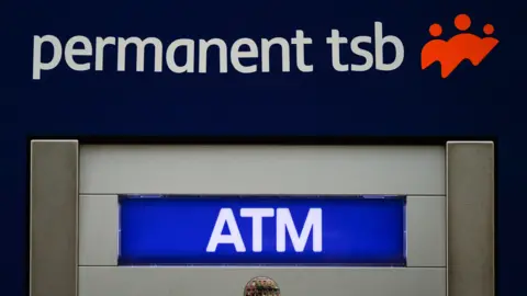 A close up of an atm. Lettering states permanent tsb ATM. A red logo shows three people. A reflection in a small circle shaped mirror displays a street. 