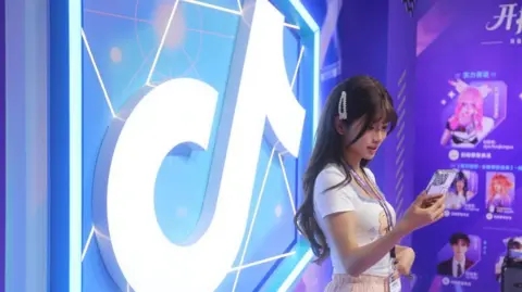 Woman standing in front of a brightly-lit and colourful TikTok logo while looking at her smartphone