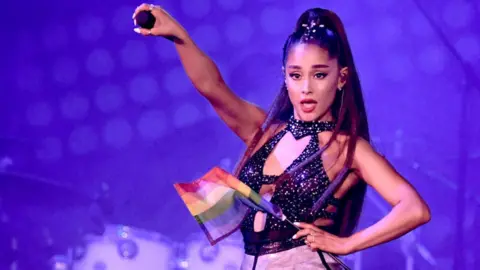 Kevin Winter Ariana Grande on stage holding a rainbow flag