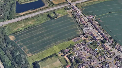 An aerial image of the green farmland earmarked for development. Next to it are lots of homes that form a village.