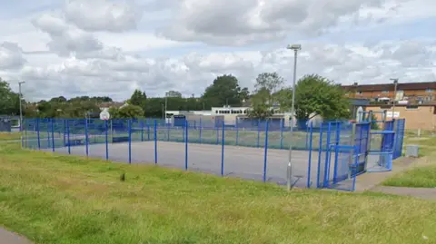 An outdoor sports pitch surrounded by blue fencing and green grass