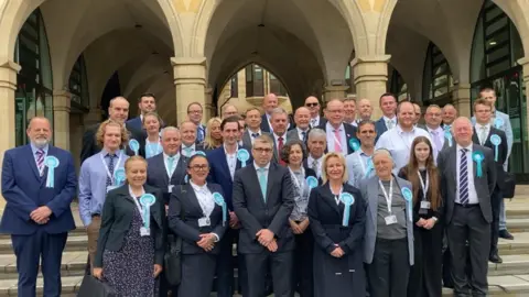 A group of Reform UK councillors most wearing suits and the party rosettes