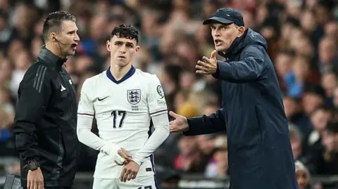 Thomas Tuchel gesticulates while standing next to Phil Foden