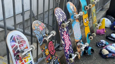Skateboards lined up against some railings with multiple colours on the base of the decks.