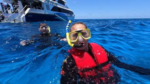 Will Rotheram A selfie of Will and Laura in the water while snorkelling. They are wearing snorkelling gear, life jackets, and the sea is a beautiful sapphire blue colour.