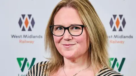 Kelly Henshall, head of performance at West Midlands Railway, seen with the company logo behind her.