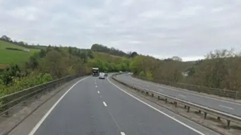 Google Street View image of the A38 near Buckfastleigh in Devon. The road is going along a bridge which is going over the town. Several vehicles are in the distance.