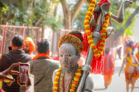 An ash-smeared ​Hindu holy ⁣man ‍holding‍ a trident at the Kumbh Mela festival in Prayagraj