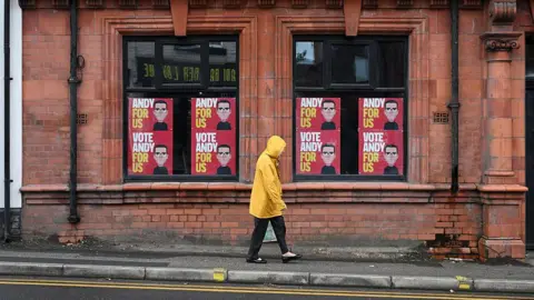 Getty Images A man walking past Andy Burnham signs