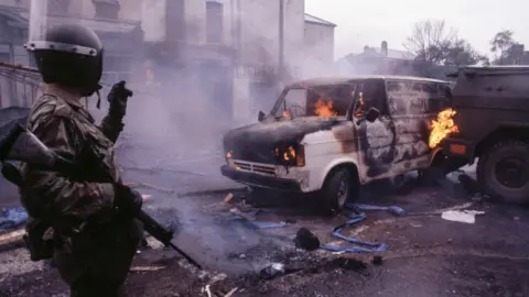 A soldier stands by a burning van in Belfast in 1981