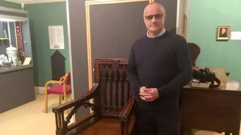 BBC Bard Tudur Dylan Jones standing next to 1819 Eisteddfod chair in Camarthen