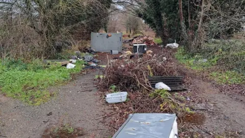 West Mercia Police A pile of vegetation/tree branches has been photographed on a muddy path with large bits of metal sheets in and amongst the greenery. 