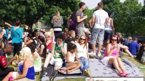 KAREN STODDART A group of people young and old sitting on a blanket on a grassy hill.