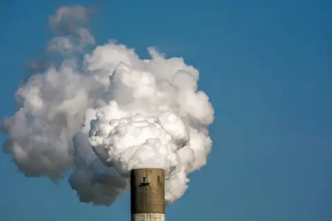 White smoke billowing out of an incinerator funnel against a blue sky.