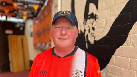 BBC/Nicola Haseler Dave Meakins wearing blue cap and Luton shirt