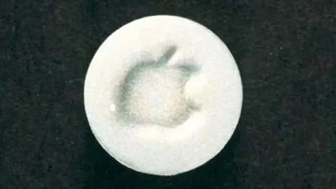 PA Media A grainy picture of a white circular tablet with an image of an apple imprinted onto it.