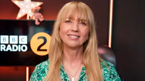 Sara Cox, wearing a green dress, in the BBC Radio 2 studio