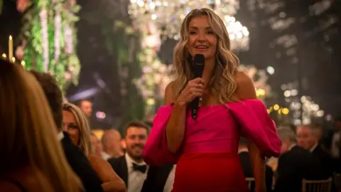 DJB Photography TV presenter Helen Skelton, wearing a red dress and addressing an audience with a microphone 