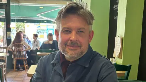 Jonathan Ashworth in a coffee shop in Leicester, with some customers in the background.