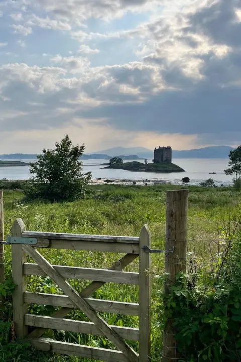 Joanna Murray A wooden gate in a field looking onto a castle on an island in the distance