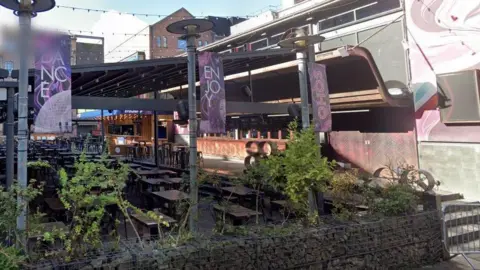 Soho bar which has a large outdoor seating area covered by a wooden roof and surrounded by a low wall made of rocks encased in wire meshing