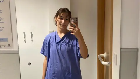 Hollie Langley A woman wearing a hospital robe taking a selfie in a mirror